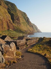 Spectacular view of the valley of the remote village of Achadas da Cruz under the steep green cliffs on the Atlantic Ocean coast at sunset, Madeira Island, Portugal.