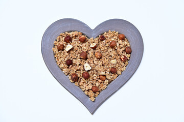 granola with whole hazelnuts in a heart shaped frame on a white background