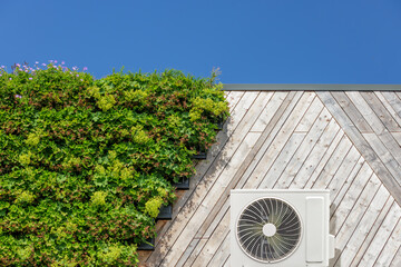 Air-source heat pump on a green sustainable building covered with blooming vertical hanging plants