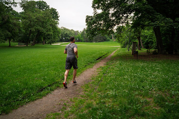 Back view, man runner in beautiful green park, running on trail 