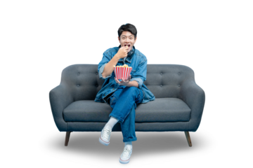 young Asian man eats popcorn while sitting on a sofa, enjoying a movie night at home. Isolated on a PNG background.