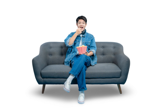 young Asian man eats popcorn while sitting on a sofa, enjoying a movie night at home. Isolated on a PNG background.