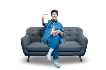 A friendly young man with popcorn on his lap holds up a smartphone with a blank white screen,...