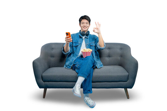 A happy man on a sofa holds a phone and gives an "OK" gesture, indicating satisfaction with a mobile app or streaming service.PNG