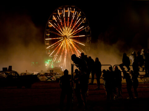 Silhouetted spectators watching a demolition derby with ferris wheel