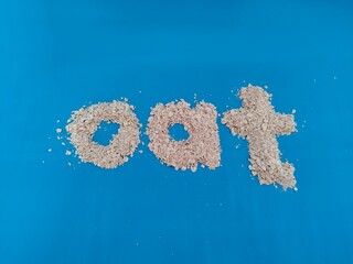 Fototapeta premium Word ‘oat’ spelled with raw oatmeal flakes on a vibrant blue background, symbolizing healthy breakfast and natural food ingredients. health, diet concept