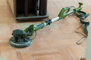 Wood Floor Sanding Process with Green Power Sander and Vacuum. Dust Removal Renovation, Interior Home Improvement, Bright Room, Close-up View