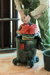 Professional Construction Worker Cleaning a Dusty Workshop Floor with a Red Shop Vacuum Cleaner,...
