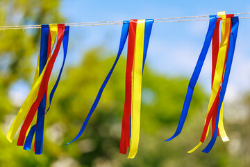 Vibrant red, yellow, blue ribbons hanging outdoors against green background