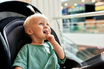 Close-up portrait of a baby in a carriage. Cute little blonde girl in green clothes is naughty, and...