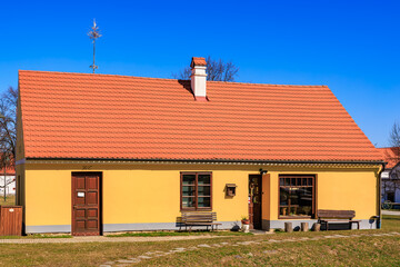 Charming small yellow house with red roof in sunny countryside setting under clear blue sky