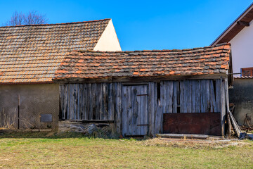 Weathered wooden barn in rural landscape with tiled roofs under blue sky