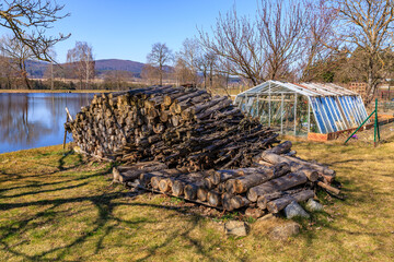 Woodpile beside lake with greenhouse and scenic landscape
