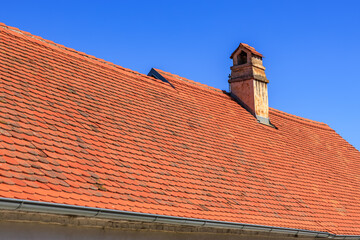 Red tiled roof with chimney under clear blue sky