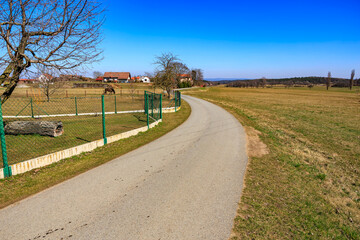 Curved rural road with fences and farmhouse in countryside landscape on sunny day