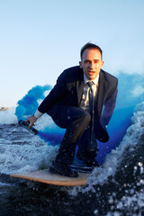 Young man surfer in classic suit with blue smoke bomb in his hand rides on the wave. Happy clerk...