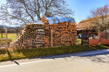 Rustic woodpile with tarp in countryside next to road on sunny day