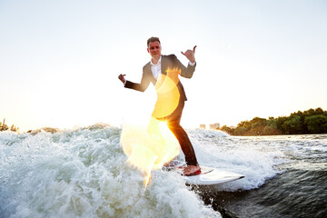 Young man in classic suit rides a wakeboard on the river or lake near city. Clerk escaped from a...