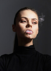 Confident young woman exhaling smoke while looking away, dressed in a black turtleneck pullover....