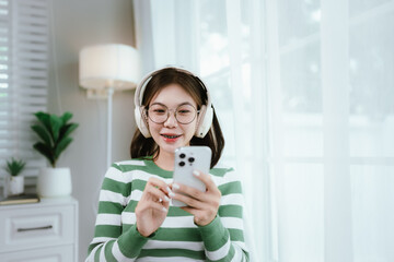 A young woman in a striped shirt and glasses relaxes indoors, enjoying music or a podcast through...