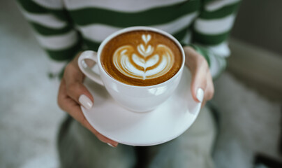 A woman enjoys a hot cappuccino, holding the coffee cup gently with both hands, savoring warmth and relaxation during a peaceful morning coffee break in a cozy café.