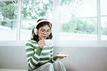 A young woman in a striped shirt and glasses relaxes indoors, enjoying music or a podcast through...