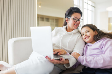 Mother and daughter enjoy quality time together while working on a laptop in a cozy living room...