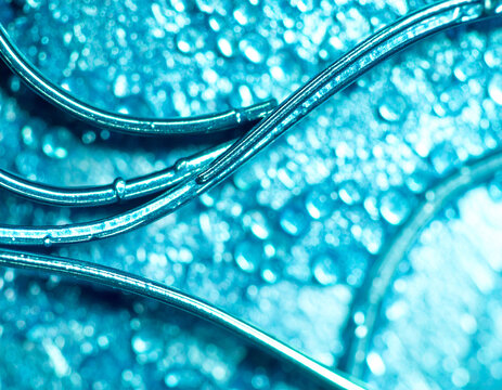 Abstract close-up view of interconnected, shiny, teal-colored tubes or wires, with water droplets.
