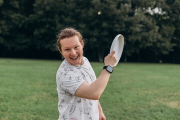 Focused portrait of male in patterned shirt with smartwatch ponytail hairstyle holding frisbee near...