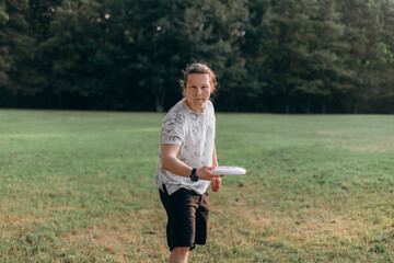 Athletic adult with tied hair bent stance preparing dynamic frisbee throw green grass background...