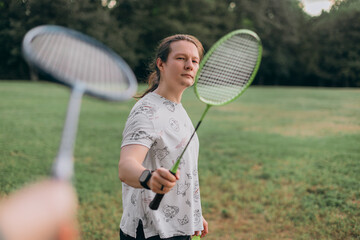 Focused male with tied hair holding green badminton racket aimed toward camera blurred opponent...