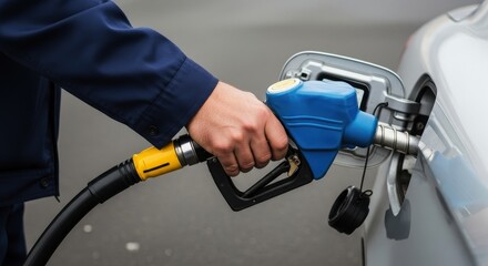 Man hand holding a blue fuel nozzle filling up a silver car with gasoline