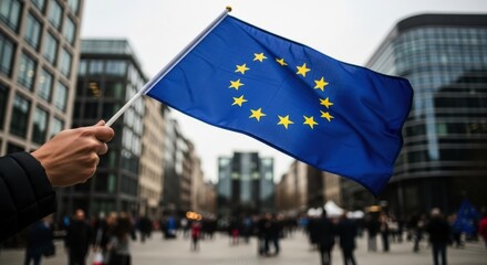 Human hand holding european union flag waving in city street with blurred crowd