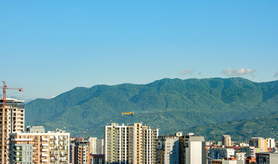 Urban skyline with mountain backdrop. Modern city high-rises set against a stunning backdrop of green mountains. The harmonious blend of urban and natural landscapes.
