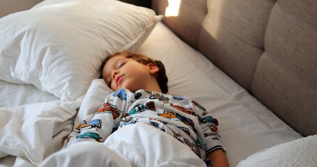 Cute little boy in pajamas with cars sleeps without pillow in spacious bed. Innocent kid immersed...