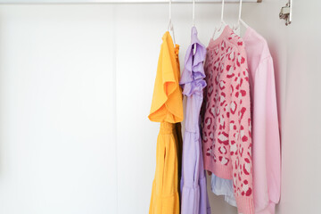 Four colorful garments hang neatly on white plastic hangers inside a minimalist white closet