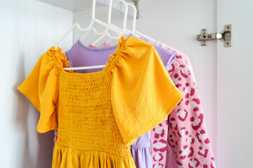 A close-up view of brightly colored children's clothes on hangers in a white wardrobe
