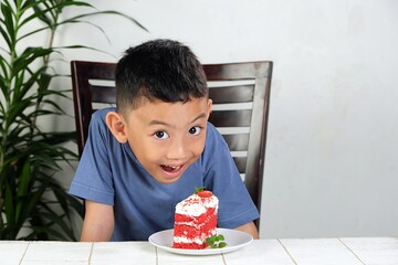 Excited young boy leans over a strawberry cake with joy, showing eagerness to enjoy the sweet dessert. A cute and playful childhood moment at home.
