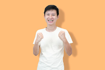 A young Asian man with braces, wearing a white t-shirt, celebrates fists and a smile against an...