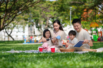 Happy Asian family enjoying a relaxing picnic together in a green park on a sunny day.