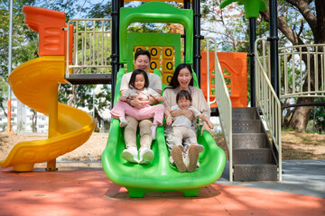 Joyful Asian family sliding together at a colorful playground during a fun day out.