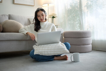 Young woman sitting comfortably on the floor with a laptop, working or studying from home in a...