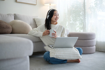 Cheerful young woman enjoying a warm drink while using laptop at home.