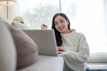Young woman smiling while using a laptop in a cozy living room with natural light.