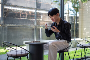 Relaxed moment of an Asian male sipping coffee and smiling, surrounded by natural light.