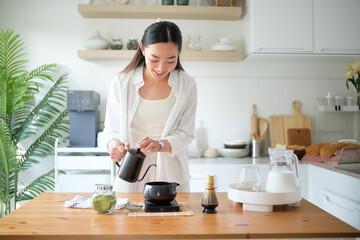 Happy female enjoying a relaxing morning ritual of preparing matcha latte in a bright modern...