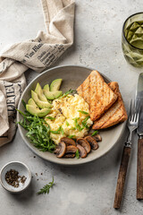 Scrambled eggs, toasts, avocado and mushrooms on rustic plate for homemade breakfast