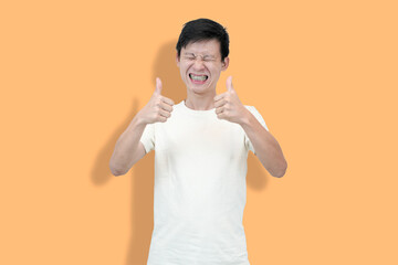 A young Asian man, wearing a white t-shirt, gives two thumbs-up with an excited, open-mouthed...