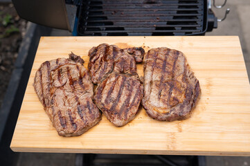 Grilled steaks resting on wooden board by outdoor grill