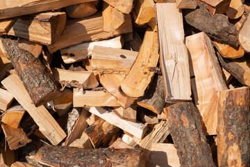 Pile of cut firewood logs with bark in outdoor sunlight